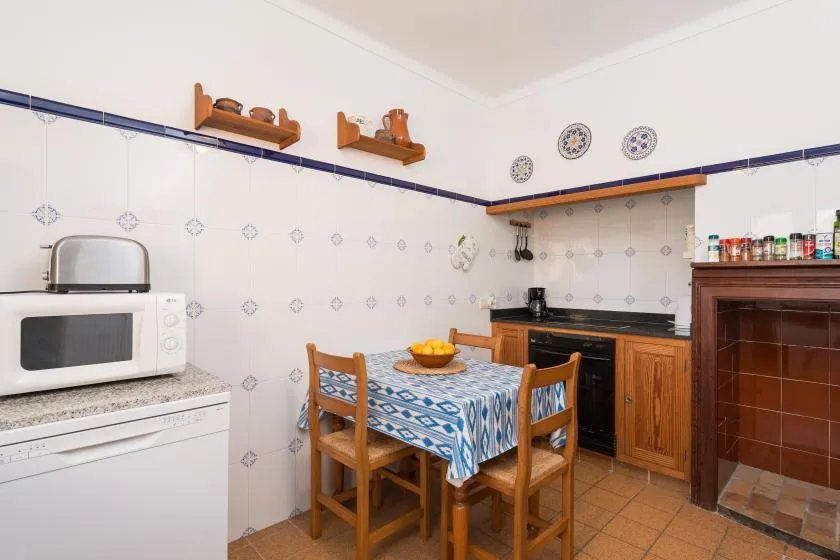 A tiled kitchen with wooden cabinets and a dining table covered in a patterned cloth.