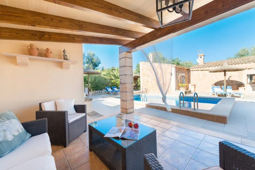 A covered patio with seating and a swimming pool in the sunny courtyard.