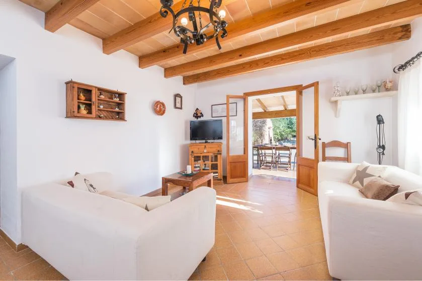 A bright living room with light-colored seating and wooden beams across the ceiling.