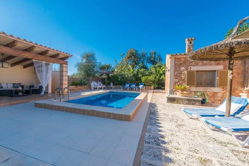 An outdoor pool sits between a covered seating area and a stone building.
