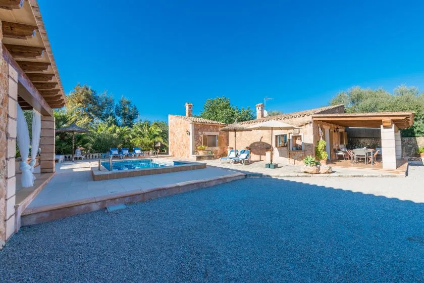 An outdoor pool and patio sit beside a low house under a clear blue sky.