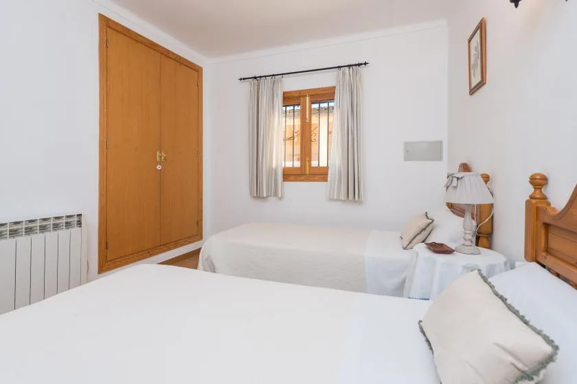 A bedroom with two beds, a wooden window, and light curtains.