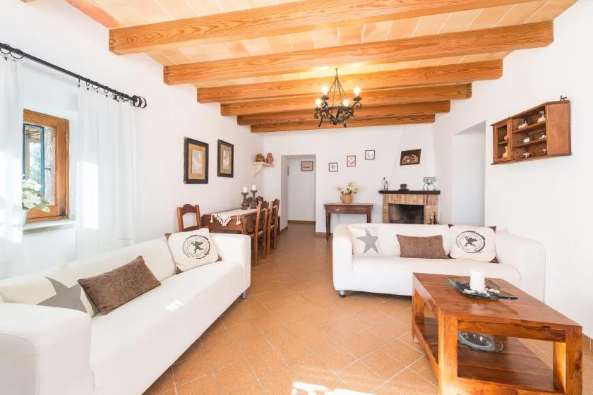 A bright living room with white seating, a wooden coffee table, and exposed ceiling beams.