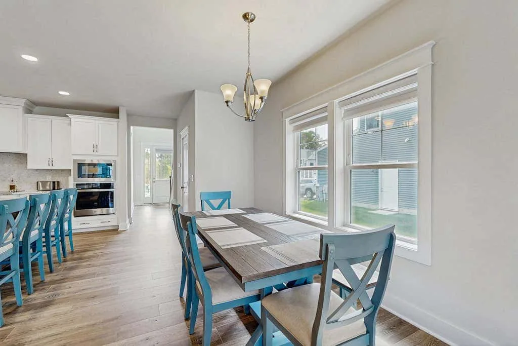A bright dining area with a long table beside large windows.