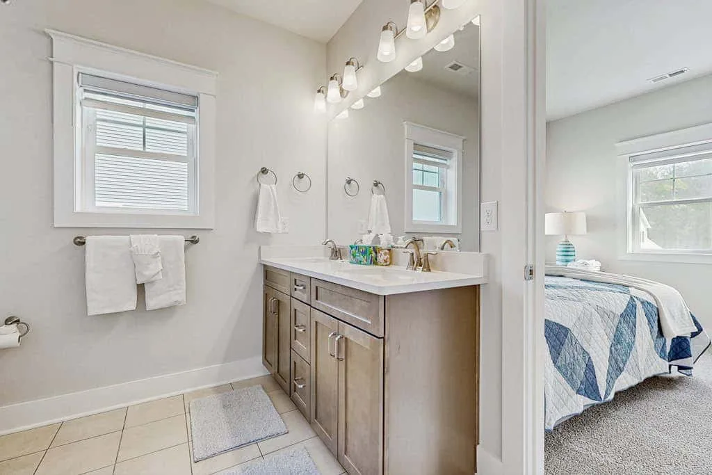 A bathroom vanity and mirror beside a bedroom with a made bed.