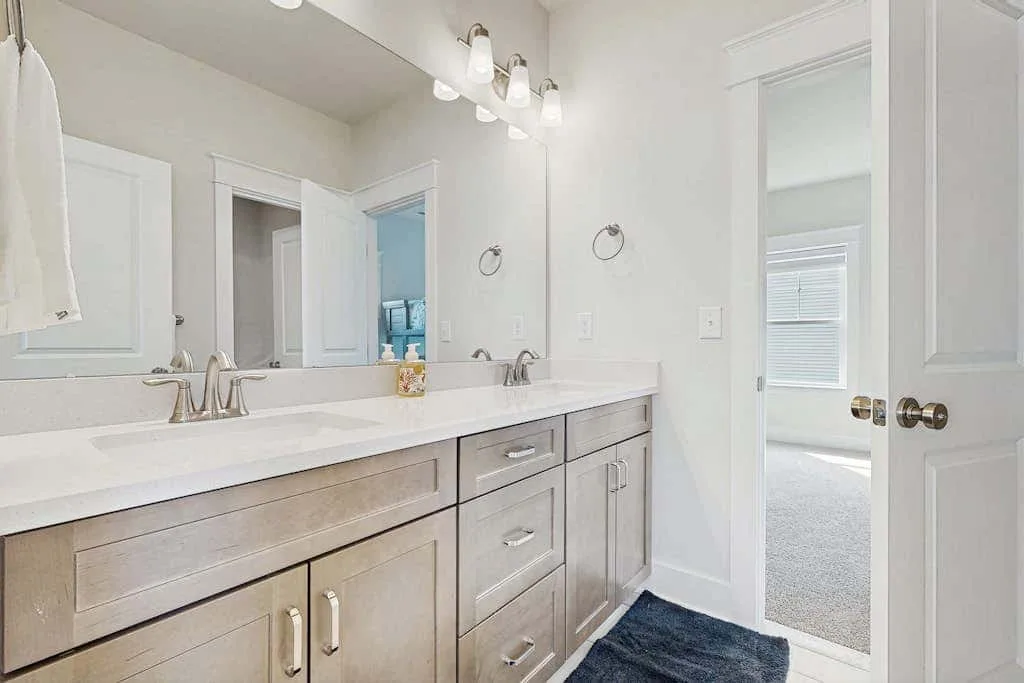 A bathroom vanity with a wide mirror, sink, and open doorway to a carpeted room.
