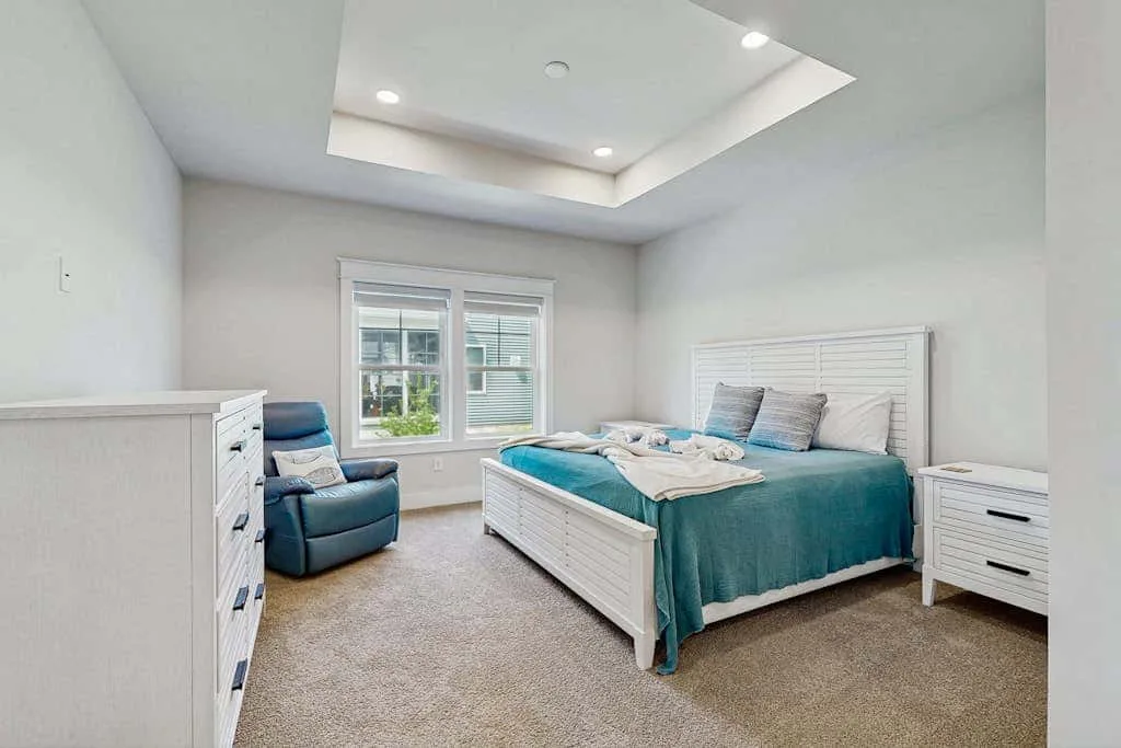 A bright bedroom with a bed, teal bedding, and a window.