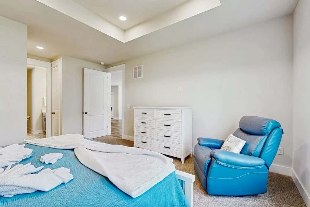 A bedroom with a blue bed, a white dresser, and a blue armchair.