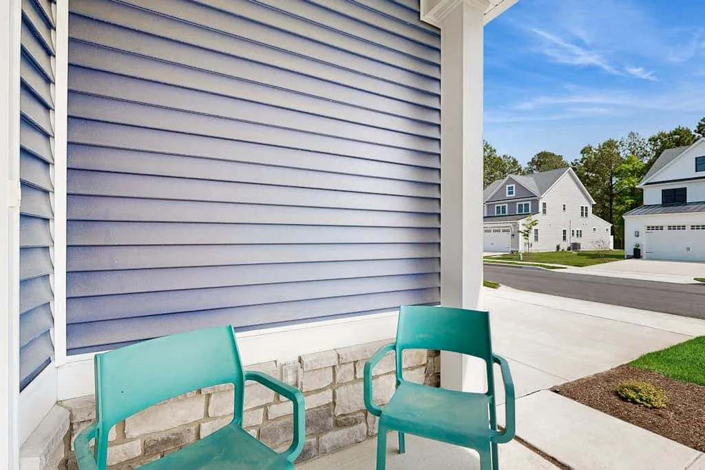 An outdoor seating area beside a house, with turquoise chairs facing the street.