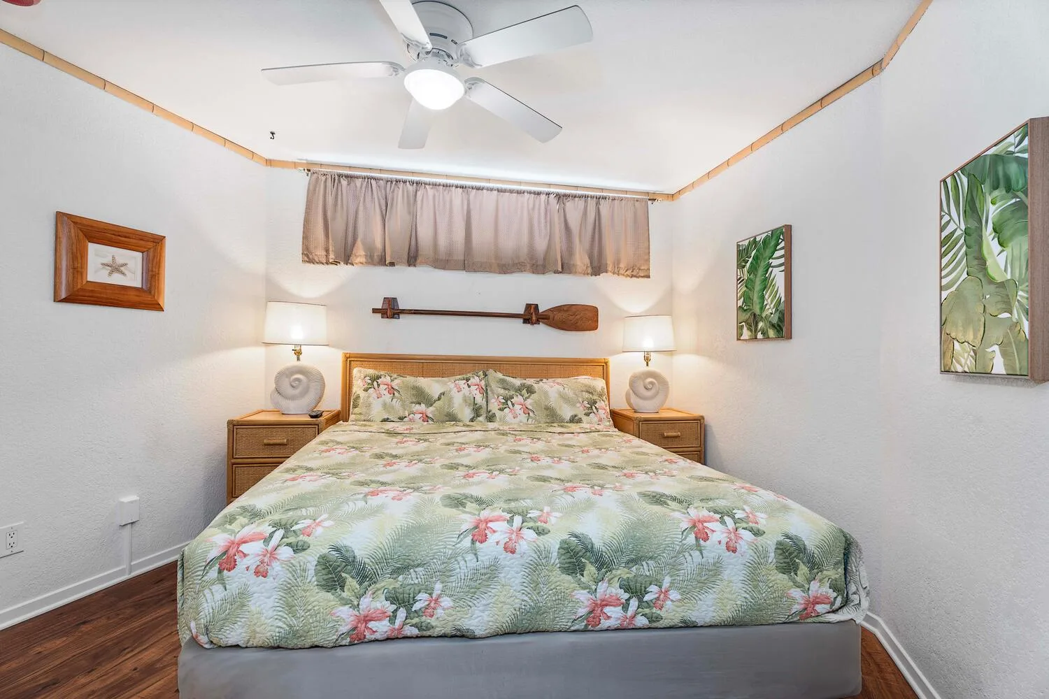 Un dormitorio con una colcha floral, mesitas de noche y cuadros en las paredes.