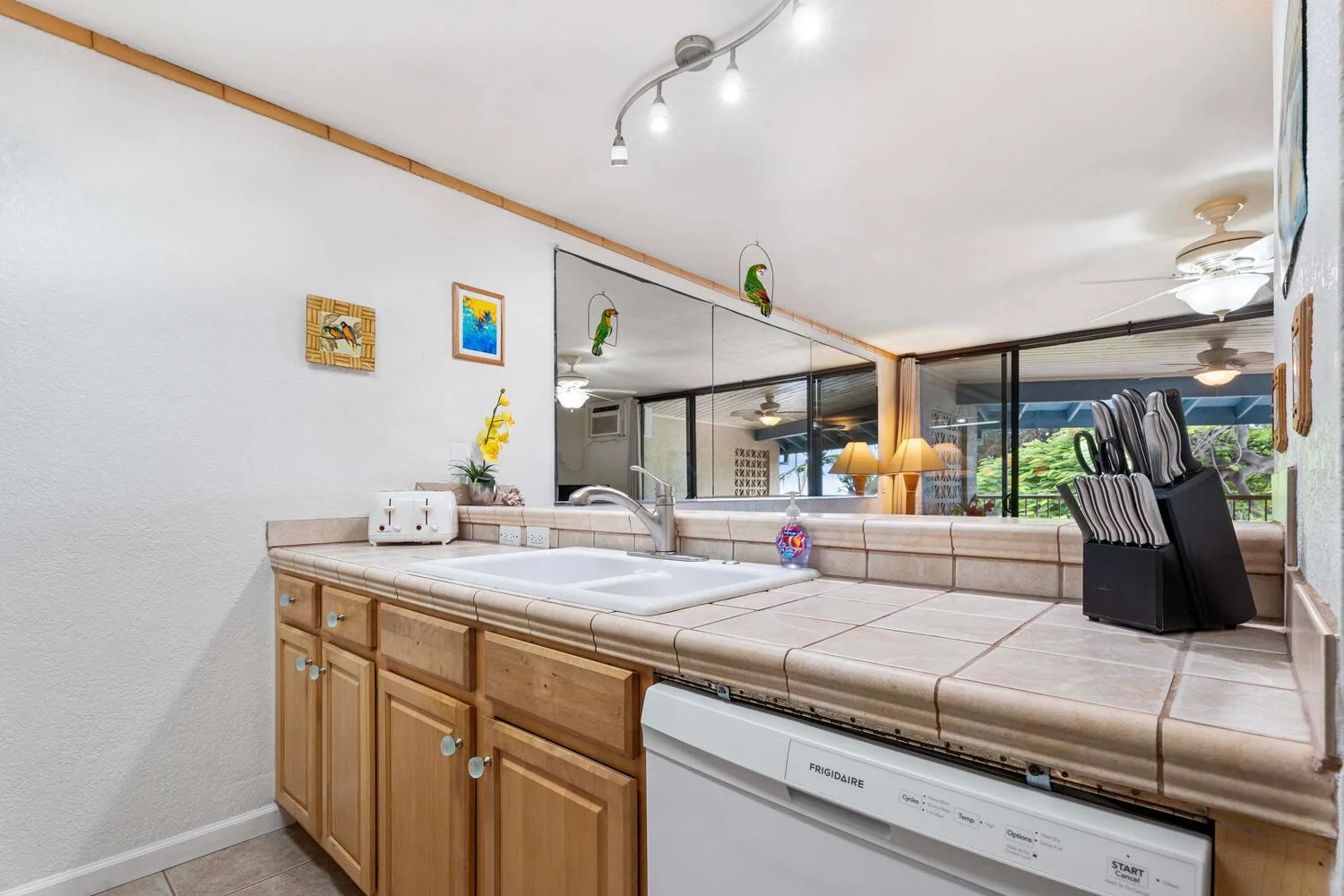 Una encimera de cocina con superficie de azulejos, gabinetes de madera y lavavajillas.