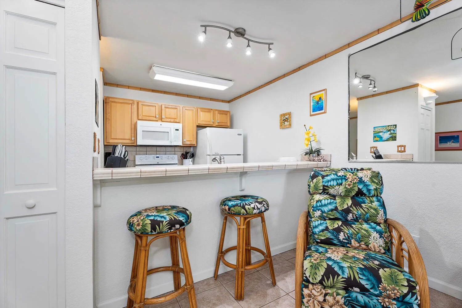 Una cocina y una barra con dos taburetes y un sillón estampado con flores.
