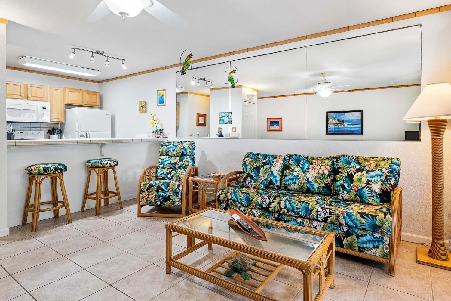 Una sala de estar con asientos estampados y una mesa de centro de vidrio junto a una cocina abierta.