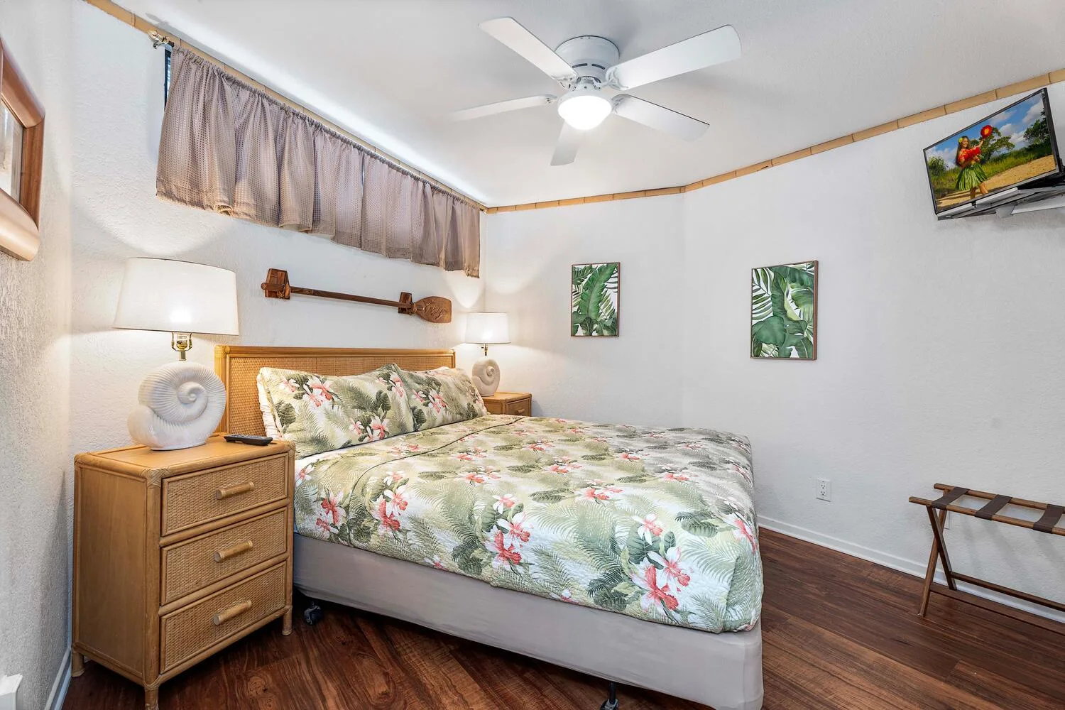 Un dormitorio con una colcha floral, mesitas de noche y cuadros en la pared.
