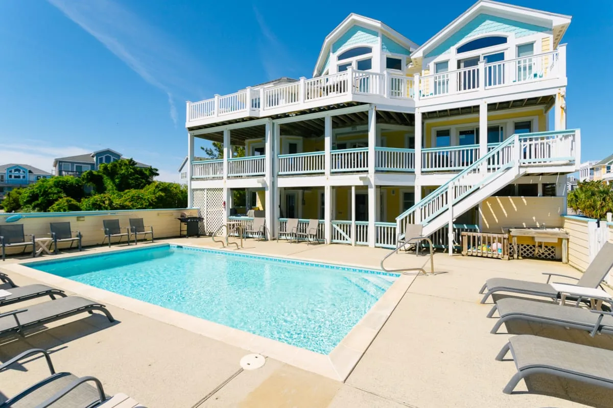 A large house stands beside a swimming pool and rows of lounge seating.
