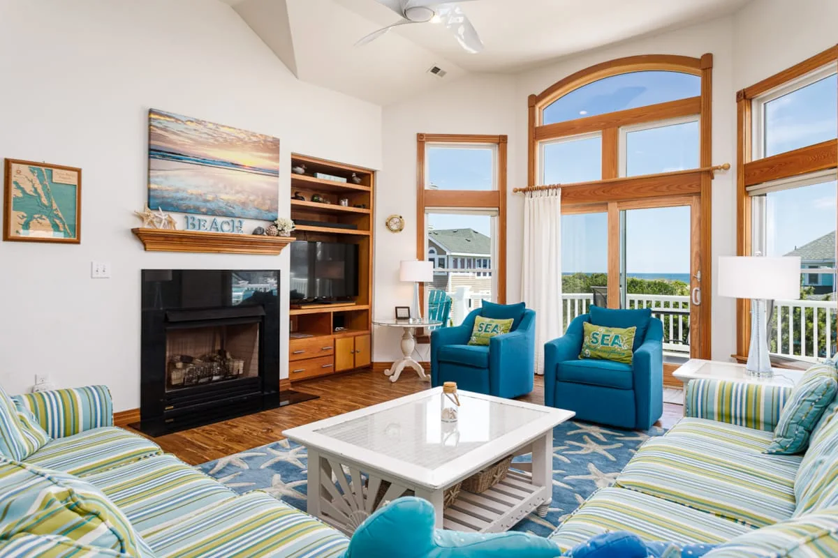 Una sala luminosa con asientos, una chimenea y grandes ventanas con vista al agua.