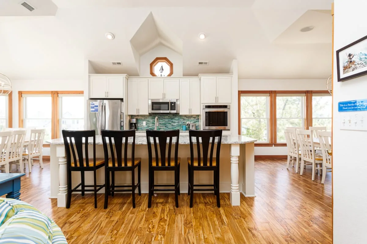 Una cocina luminosa con una isla y mesas de comedor junto a grandes ventanas.