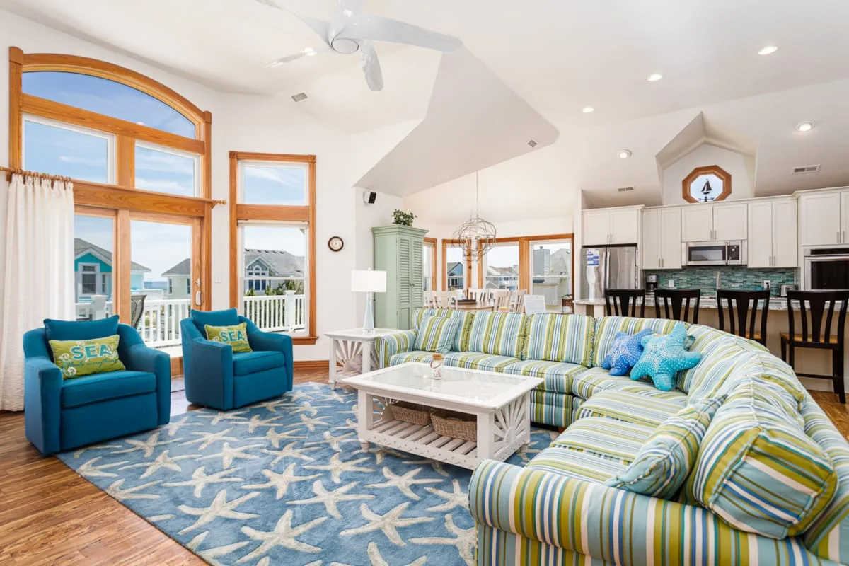 A bright living room with striped seating, blue armchairs, and a patterned rug.