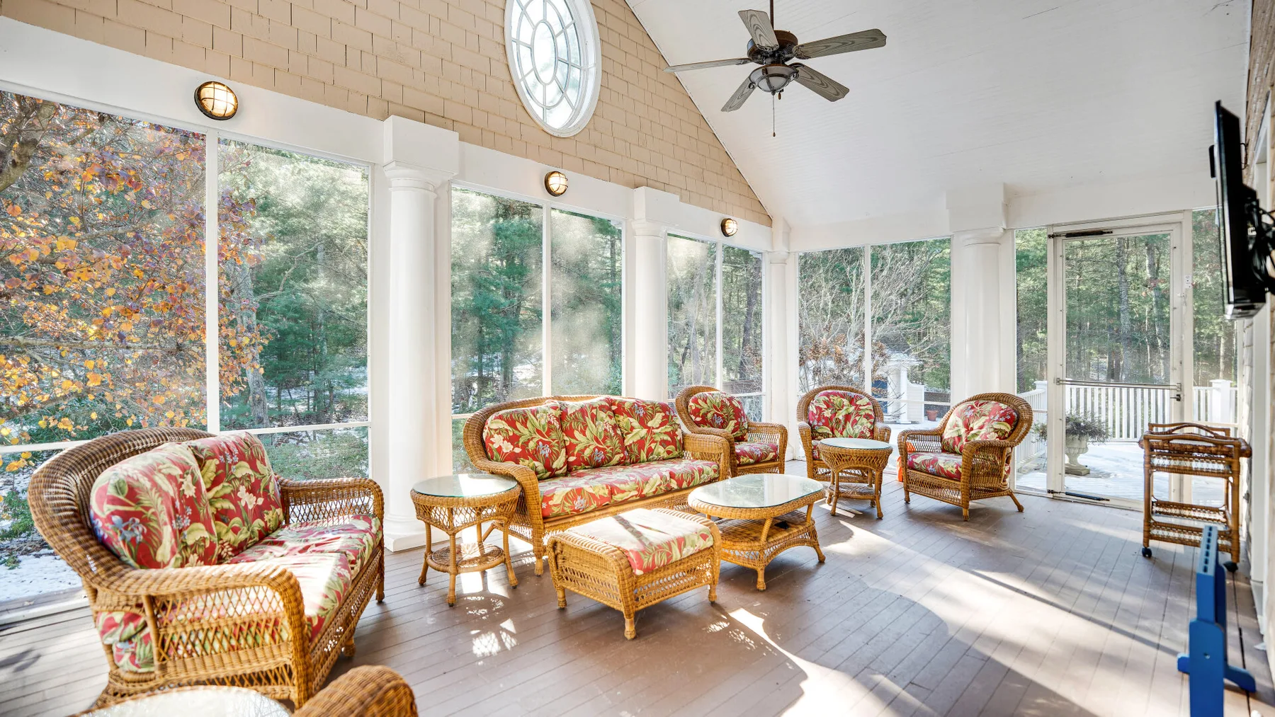 A bright sunroom with wicker seating and large windows overlooking trees.