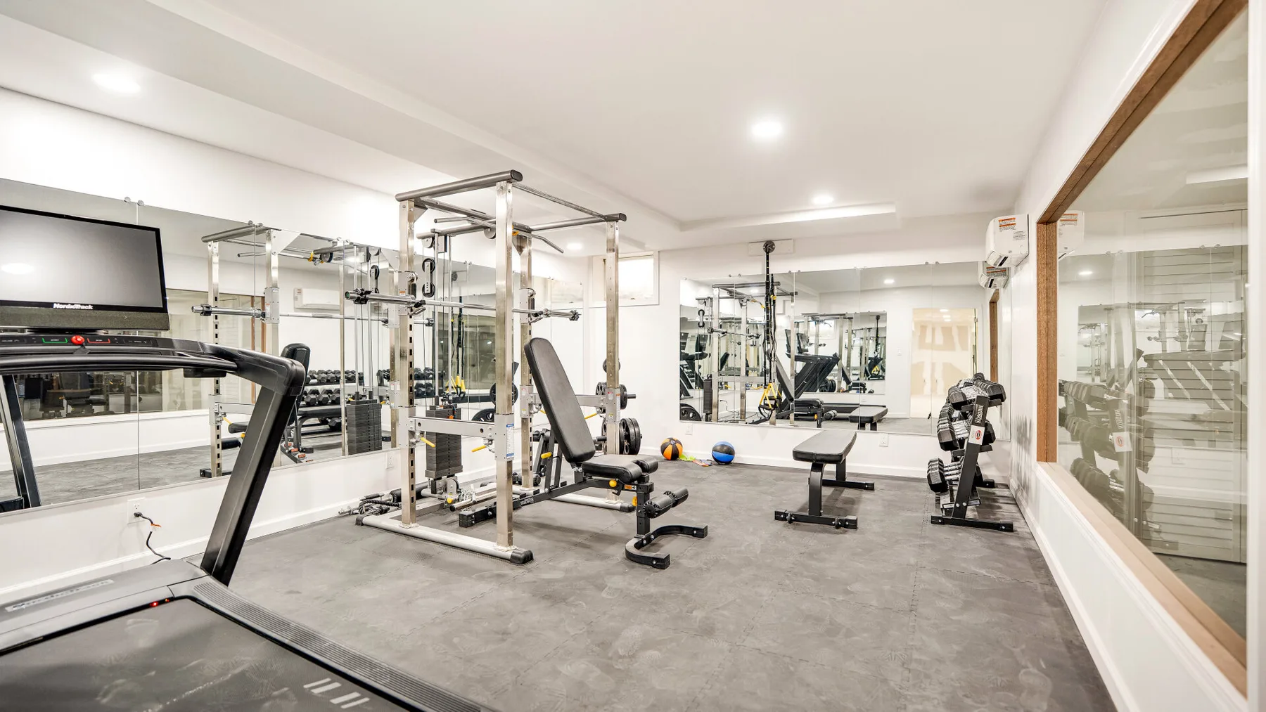 A gym with weight machines, benches, and mirrored walls.