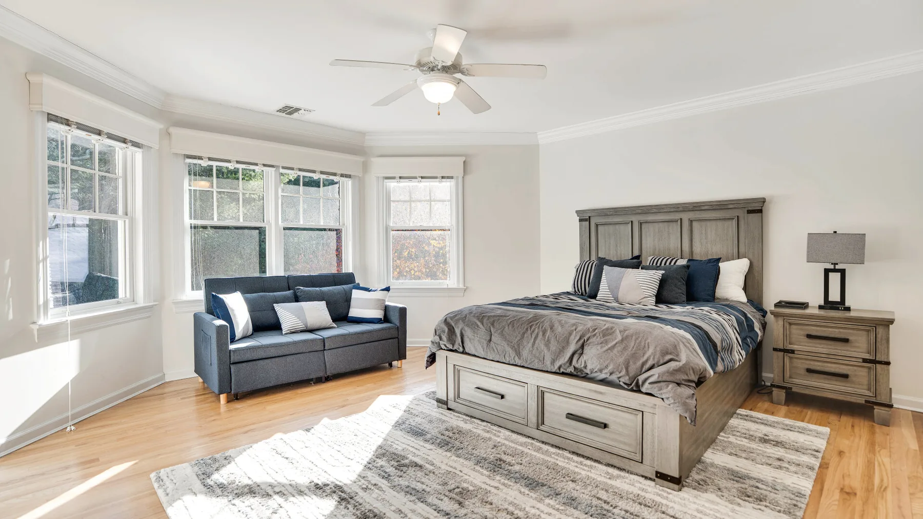 A bright bedroom with a bed, a seating area, and large windows.