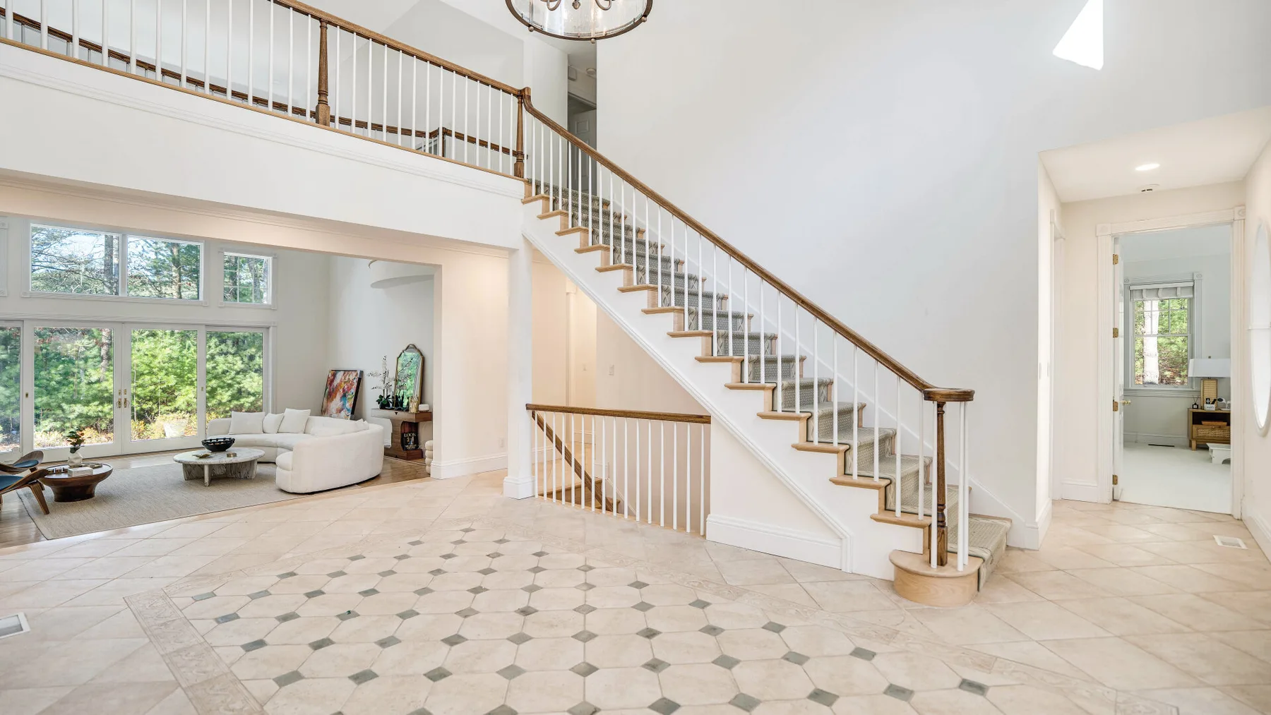A bright open foyer with a sweeping staircase and a living area beyond.
