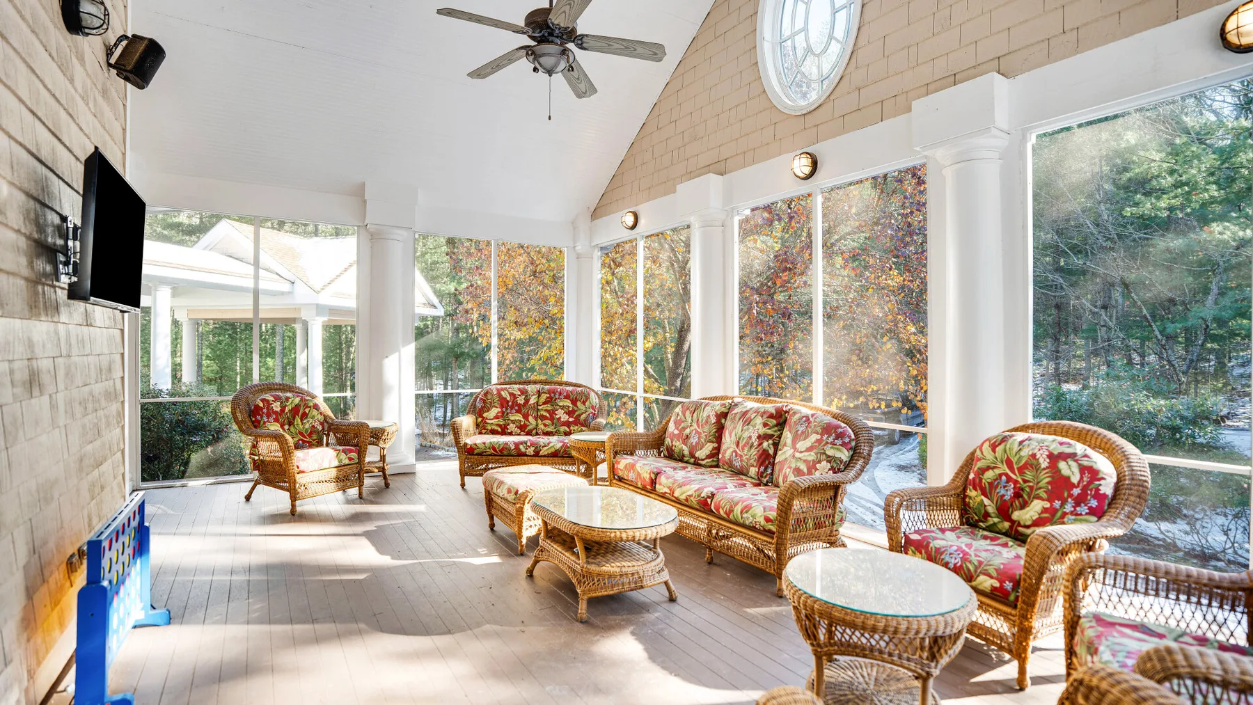 A bright sunroom with floral seating and large windows overlooking trees.
