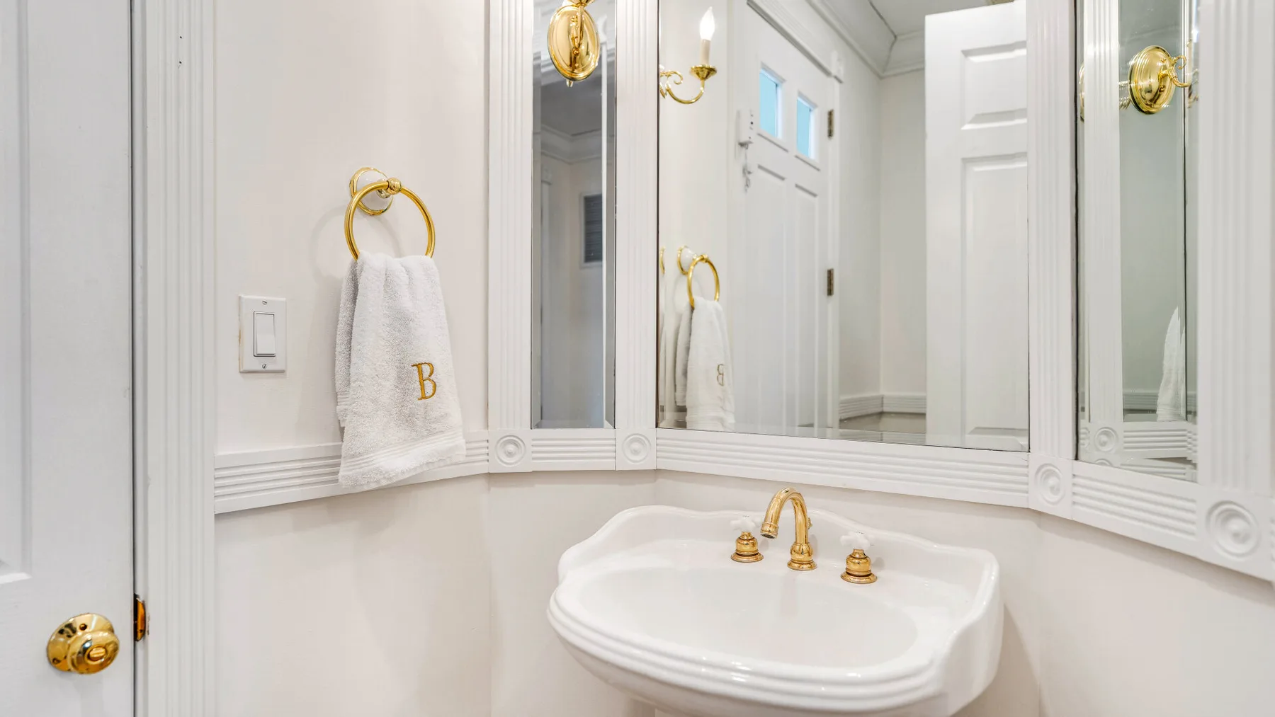 A bright bathroom with a white basin, gold faucet, and mirrored walls.