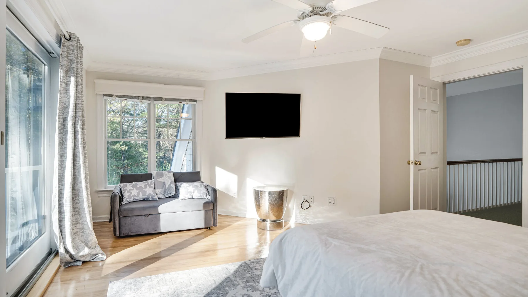A bright bedroom with a bed, a small seating area, and a wall-mounted television.