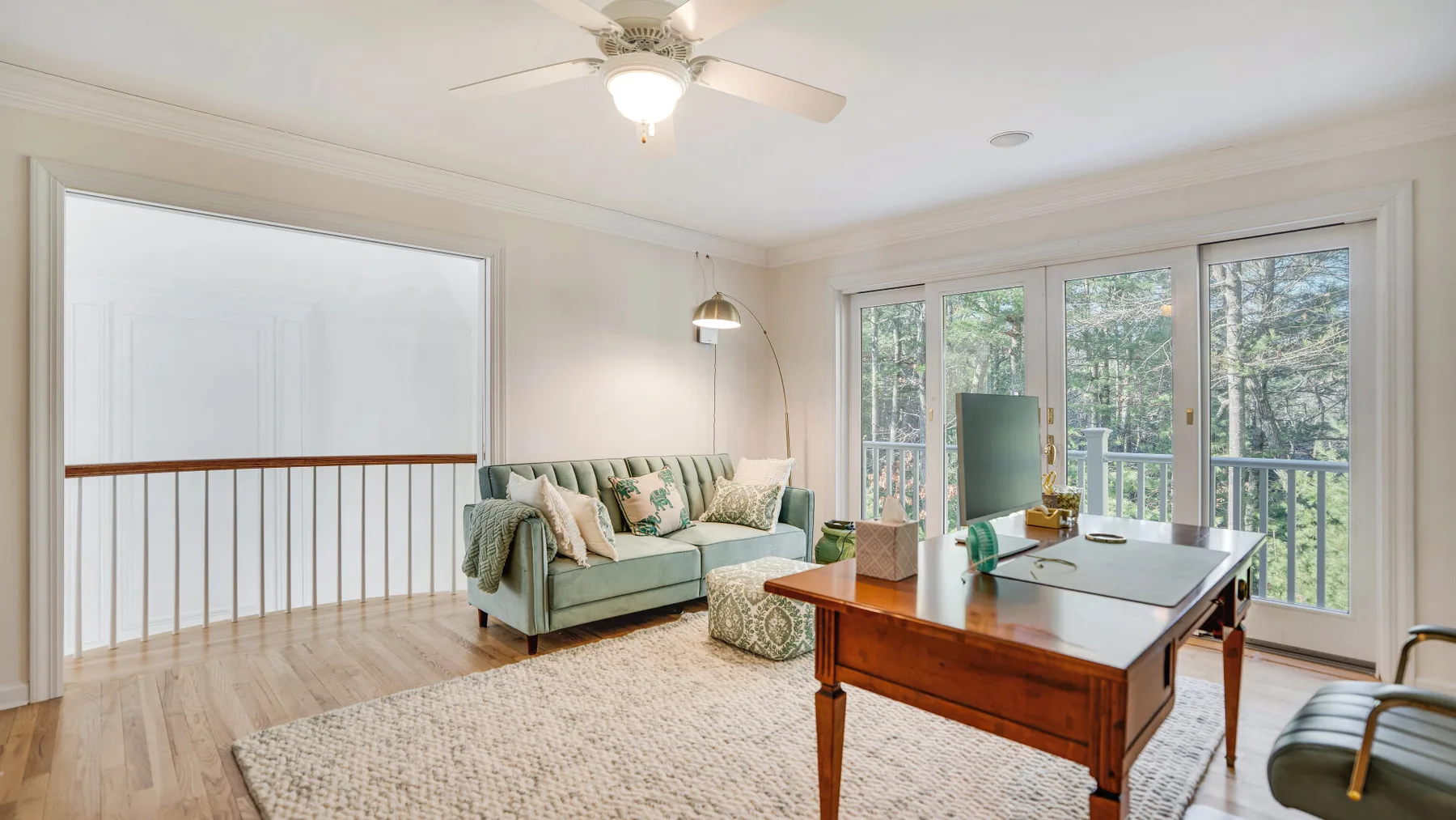A bright living room with a desk beside large windows overlooking trees.