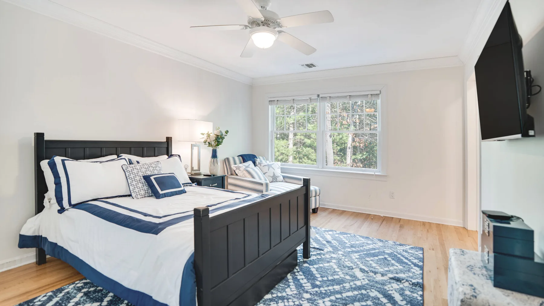 A bright bedroom with a dark bed, blue-and-white bedding, and a patterned rug.