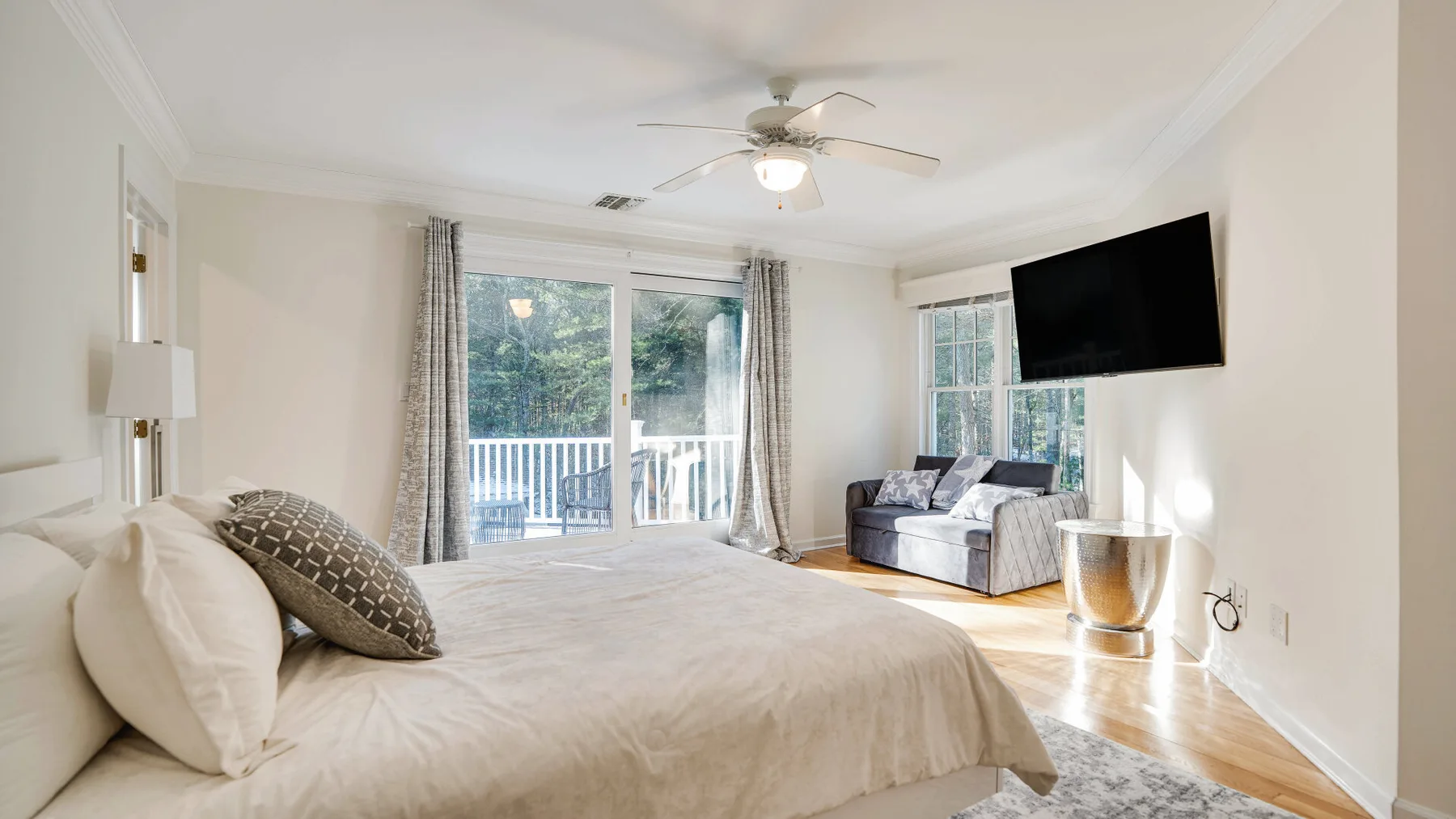 A bright bedroom with a large bed, sliding glass doors, and a wall-mounted television.