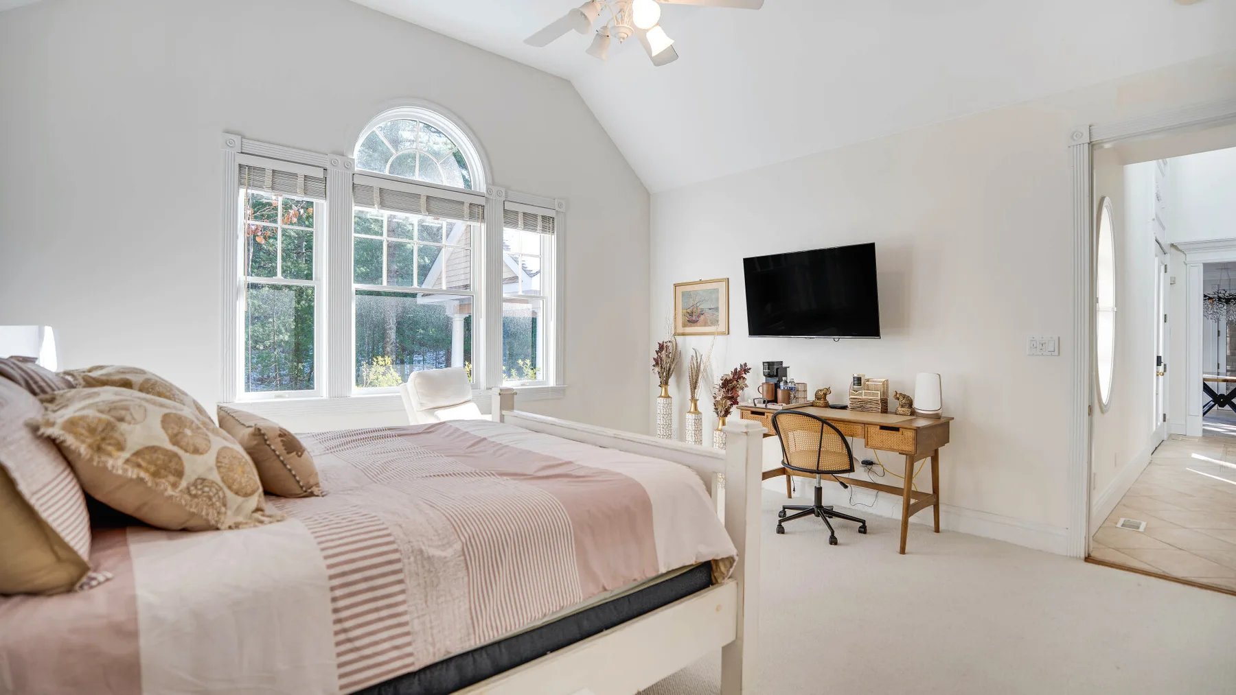 A bright bedroom with a bed, an arched window, and a desk.