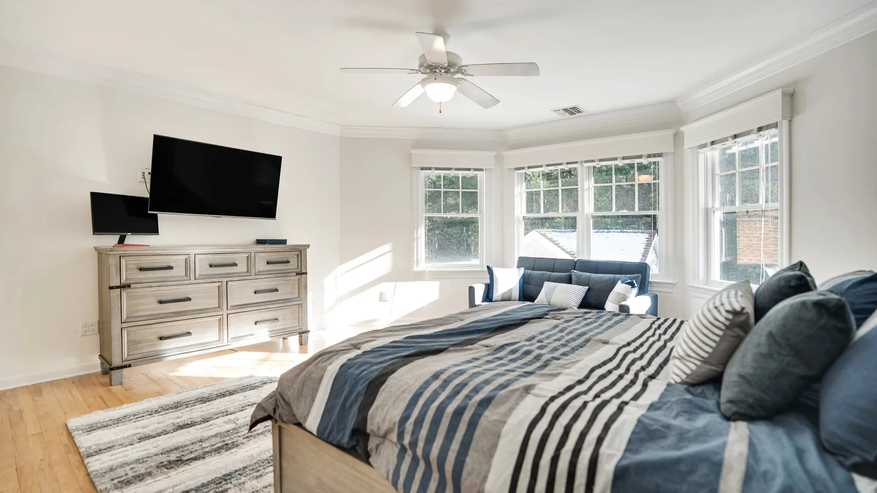 A bright bedroom with a large bed beside a bank of windows.