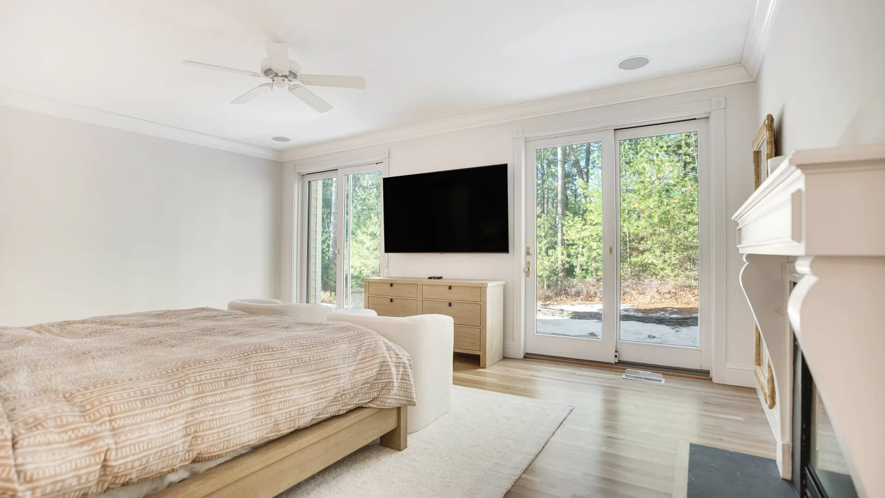 A bright bedroom with a large bed, television, and glass doors overlooking trees.