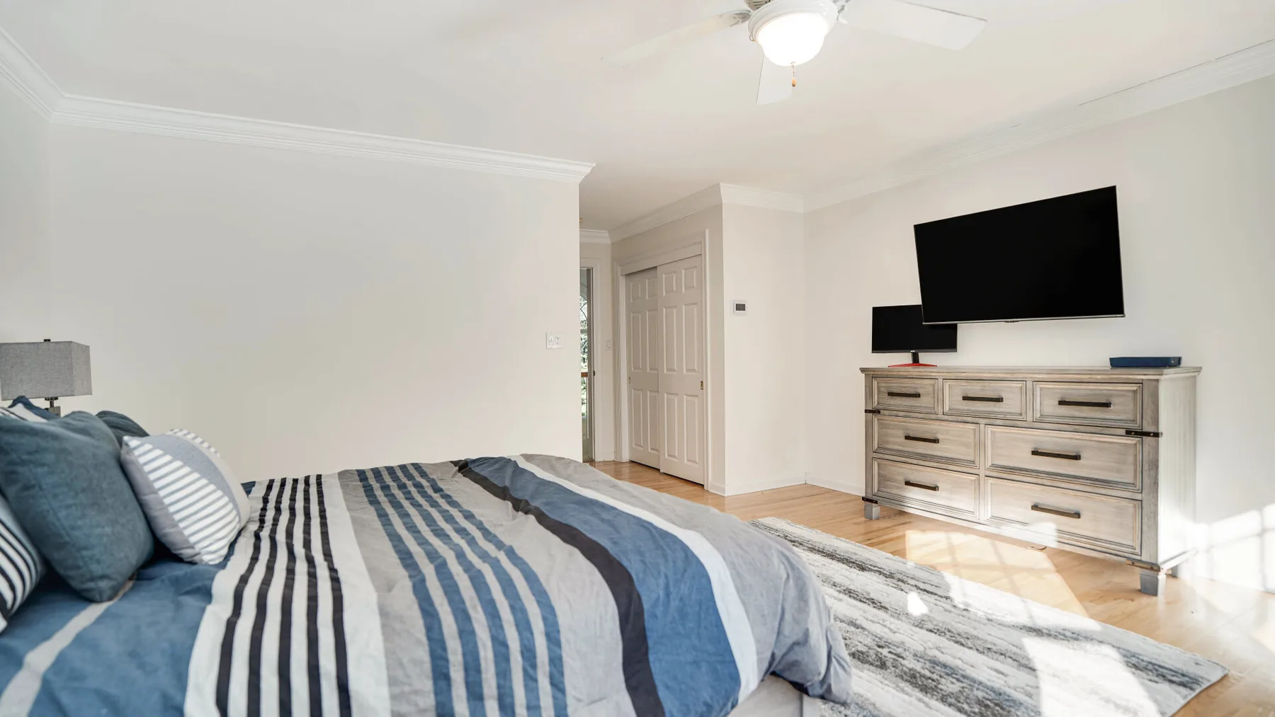 A bedroom with blue-and-white striped bedding and a dresser beneath a wall-mounted television.