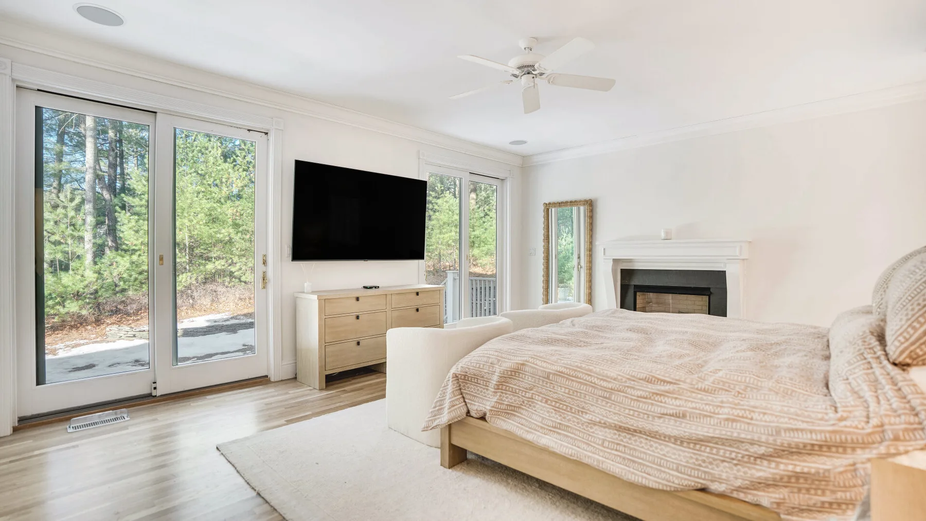 A bedroom with a bed, television, and fireplace beside large windows.
