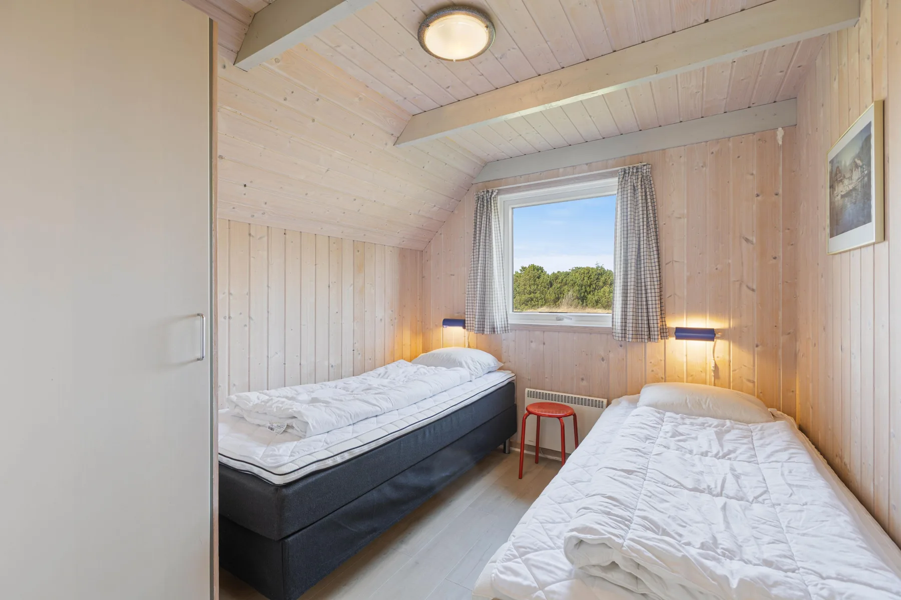 Un dormitorio con dos camas y una ventana con vistas a la vegetación.