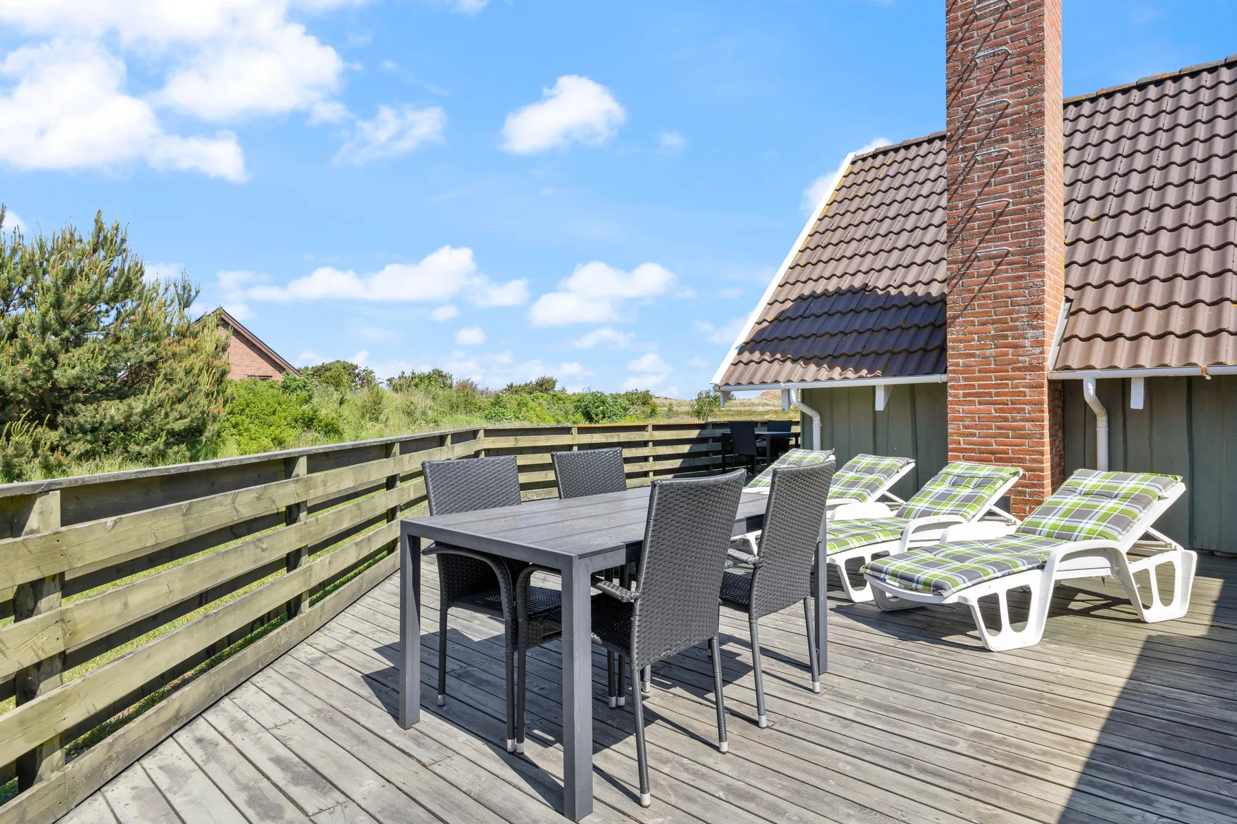 Una terraza exterior tiene una mesa de comedor y asientos junto a la casa.