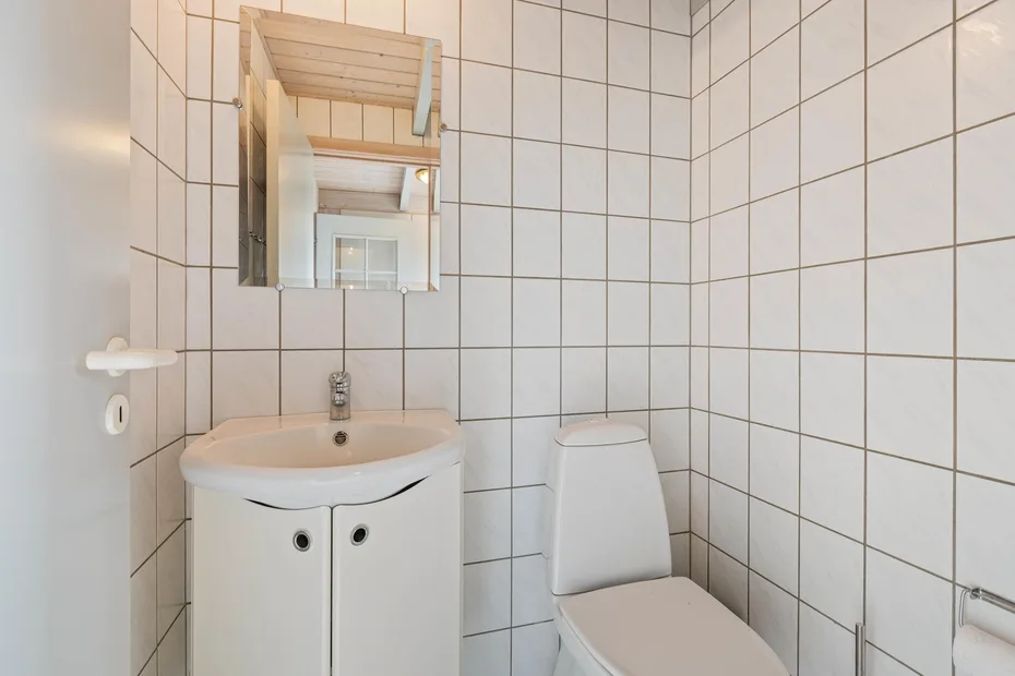 Un baño con azulejos, lavabo, espejo e inodoro.