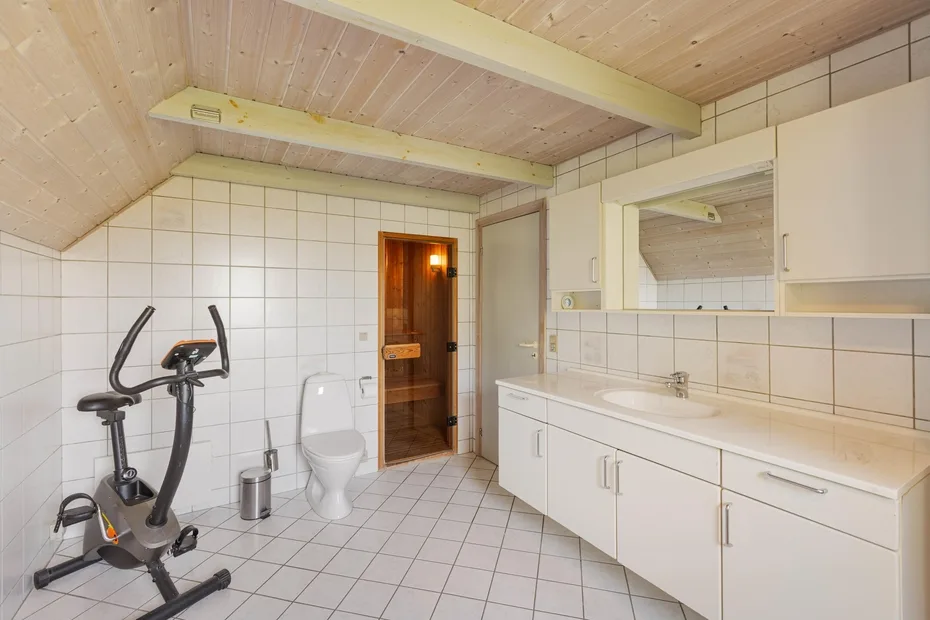Un baño alicatado con un largo tocador, espejo y bicicleta estática.