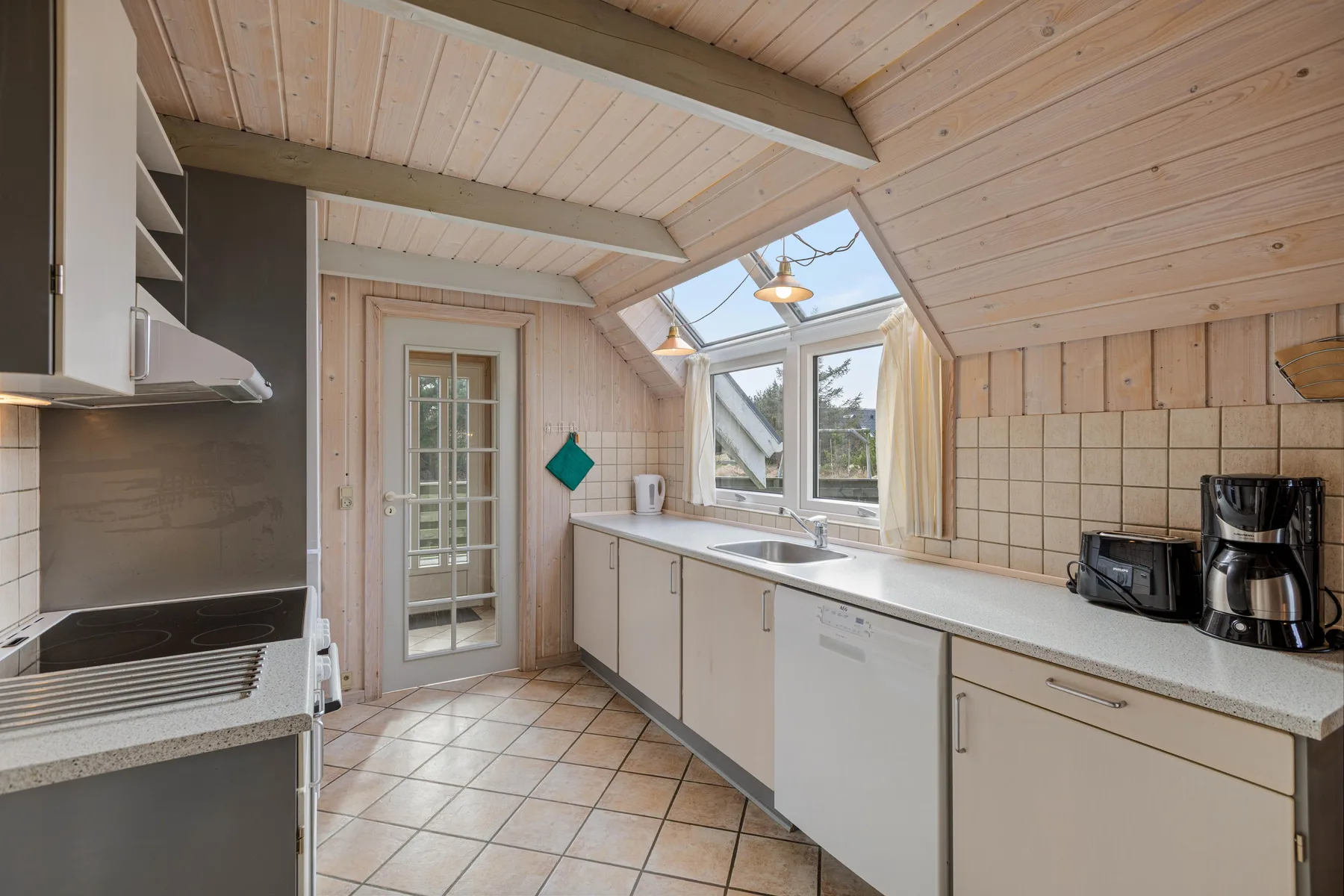Una cocina luminosa con gabinetes blancos, suelo de baldosas y ventanas en el techo.