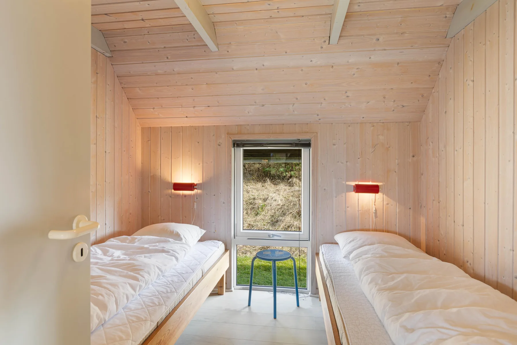 Un dormitorio luminoso con dos camas frente a una ventana y una mesita.