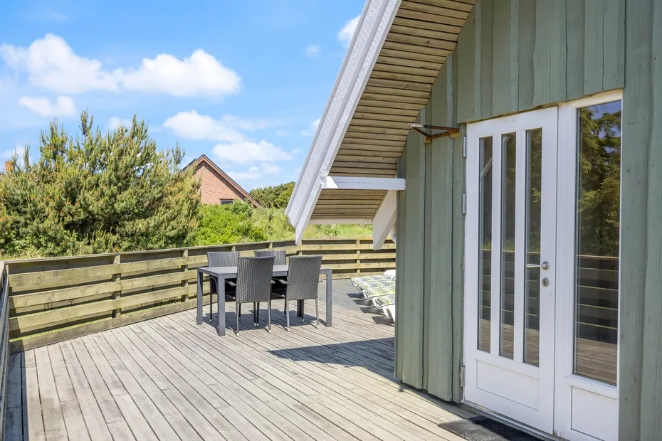 Una terraza de madera con una mesa y sillas de exterior junto a puertas blancas.