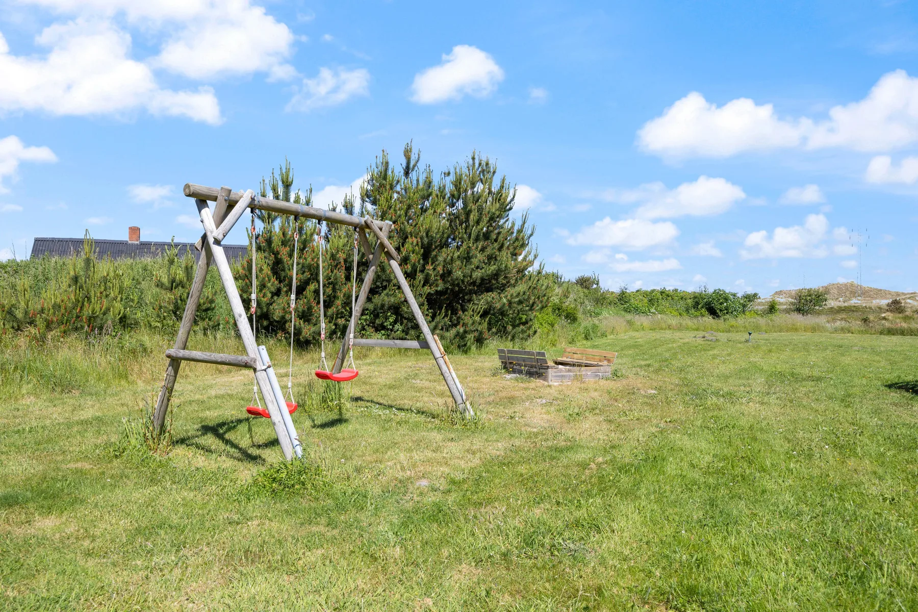 Zona de juegos al aire libre con un columpio de madera en un jardín con césped.