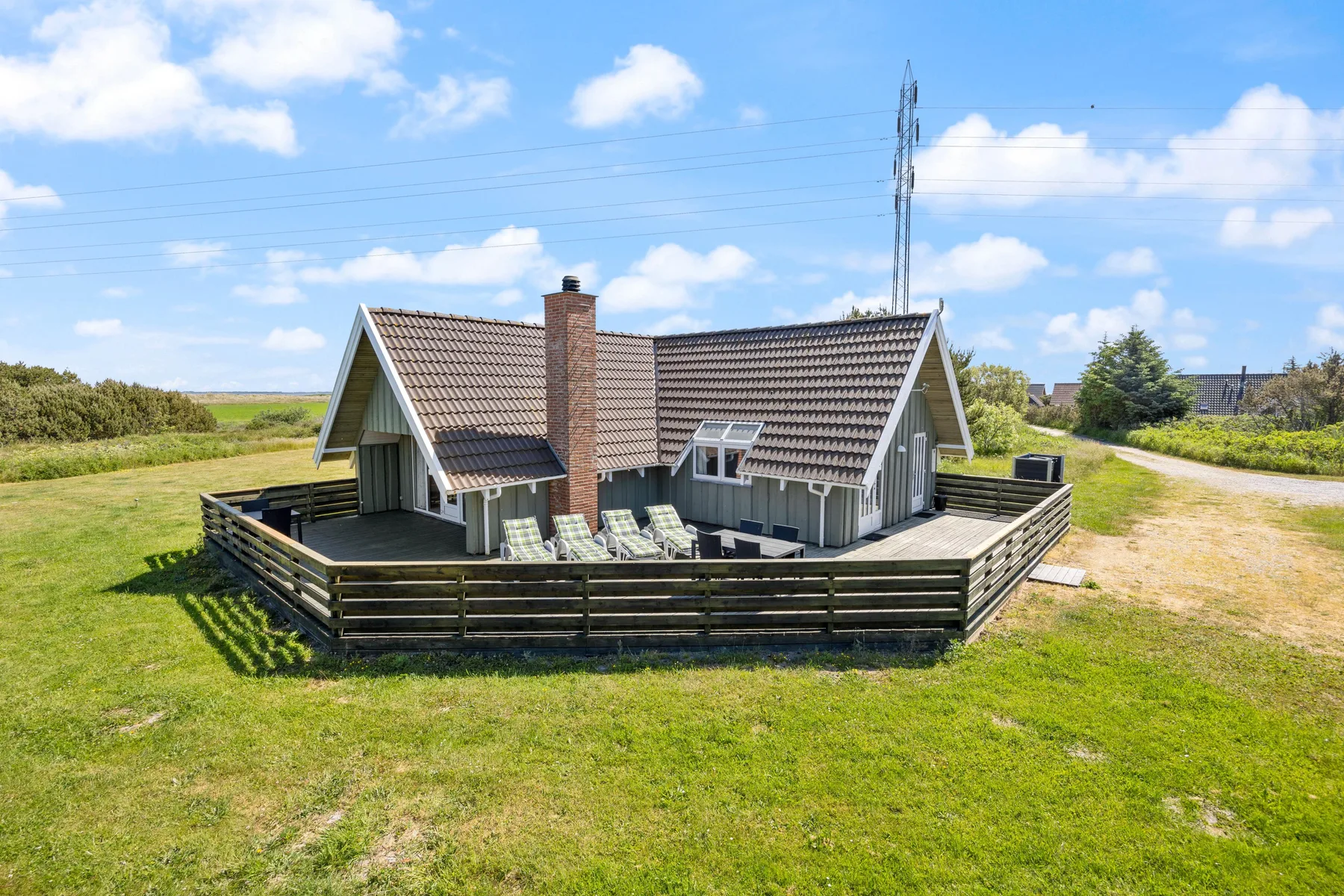 Una casa independiente con una terraza cercada se encuentra en un paisaje de césped.