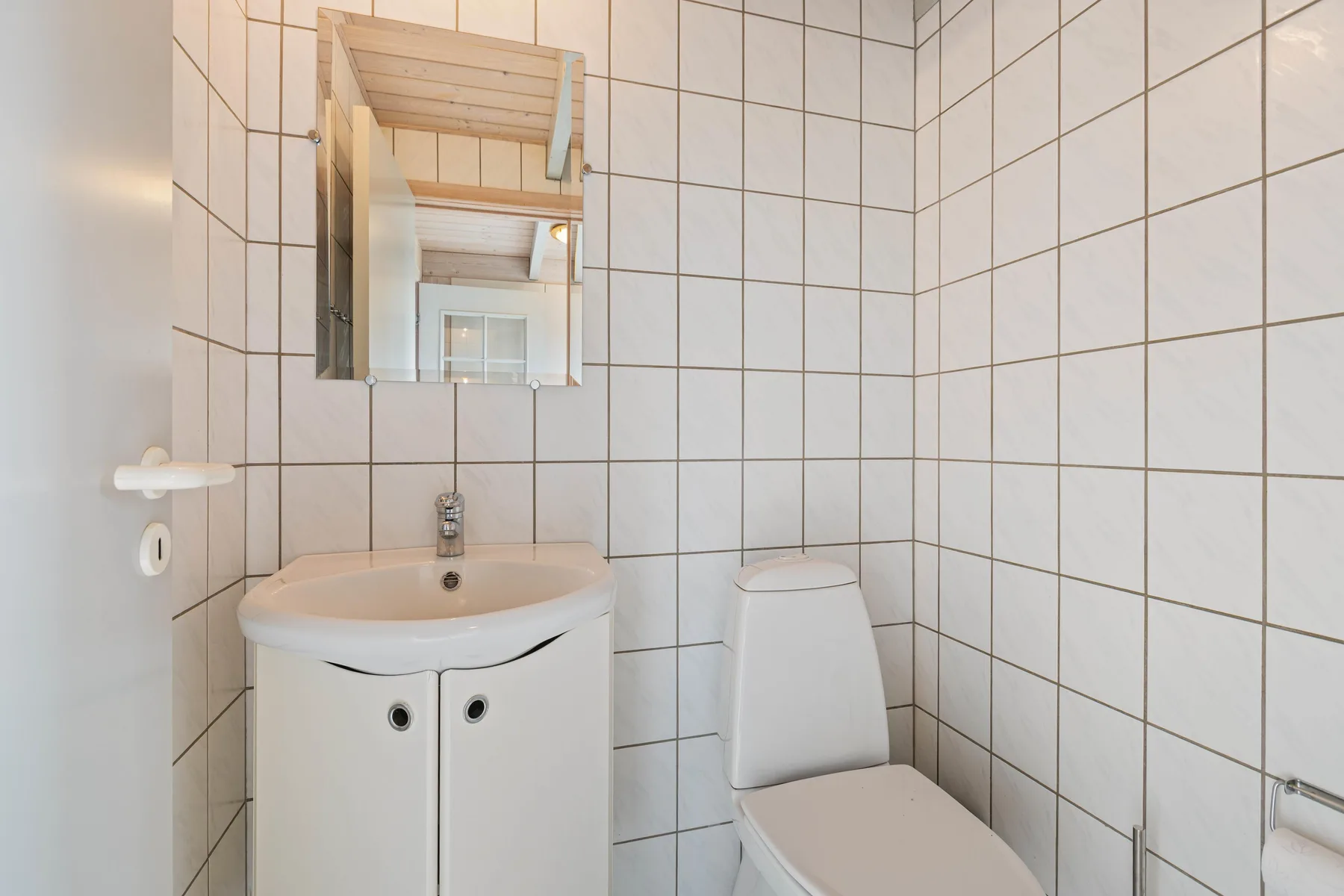 Un baño alicatado con lavabo, espejo e inodoro.