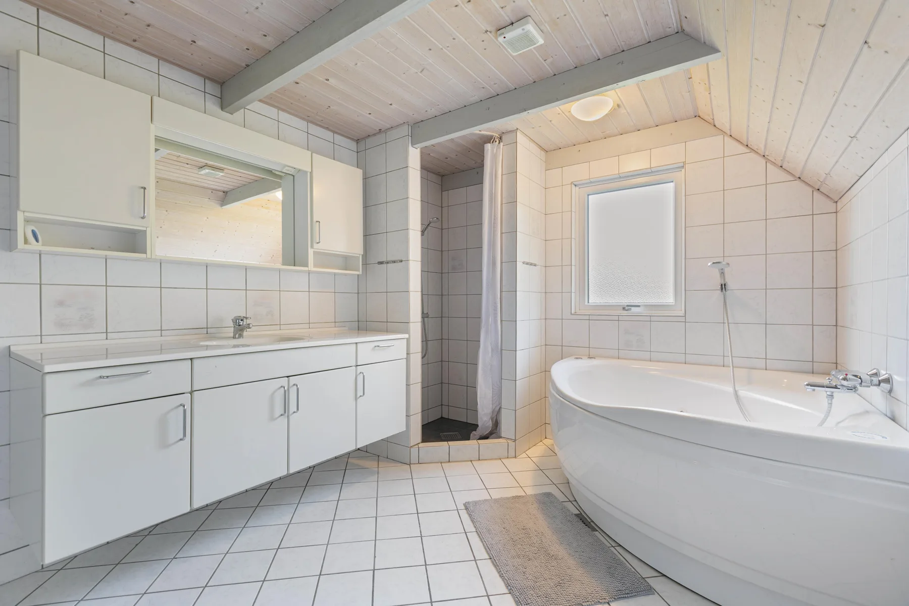 Un baño alicatado tiene un lavabo largo, una bañera y una ducha.