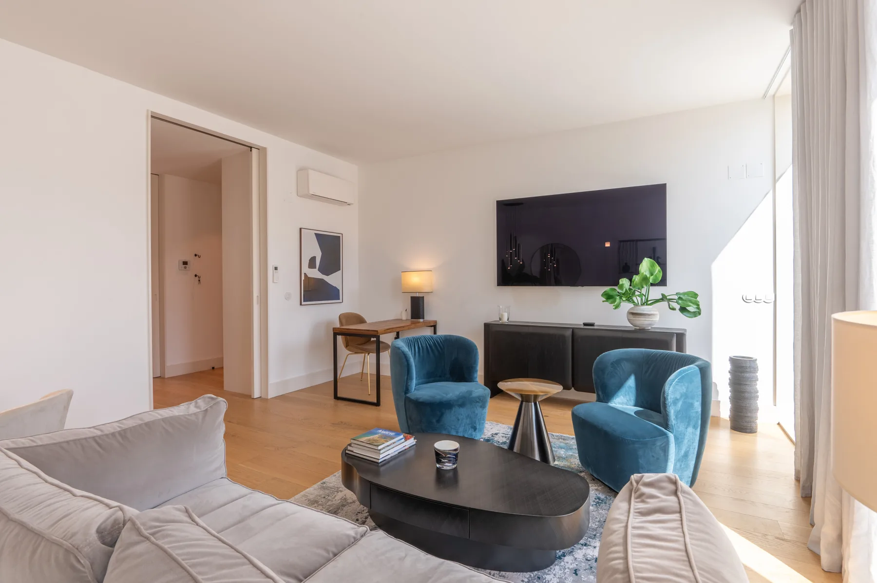 A bright living room with blue seating, a coffee table, and a wall-mounted television.