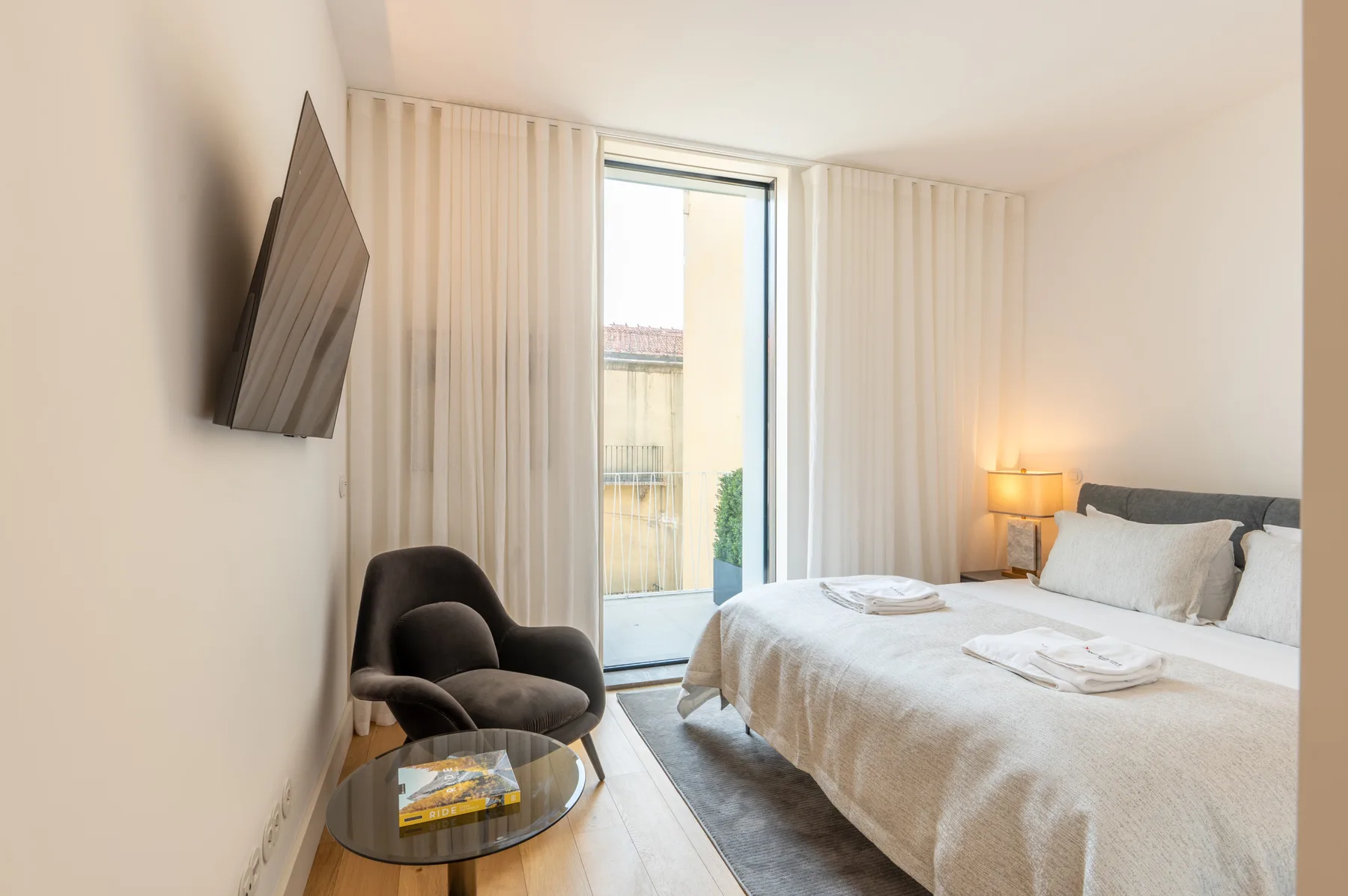 A bright bedroom with a neatly made bed and a glass door opening to a balcony.